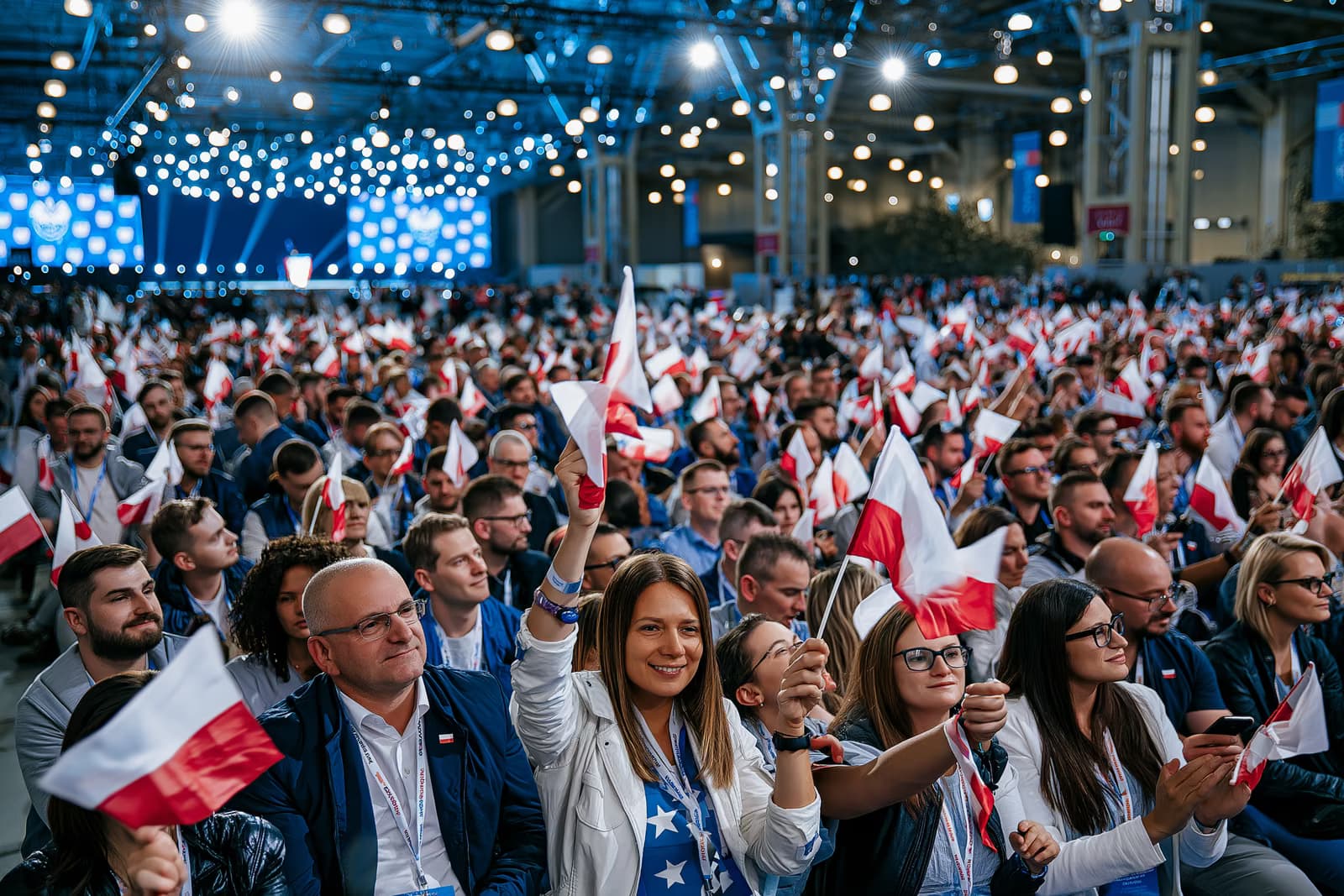Una multitud abarrotada en un pabellón de exposiciones ondeaba pequeñas banderas bajo la intensa iluminación del evento durante el lanzamiento de la campaña de AfD Magdeburgo, con un escenario al fondo.