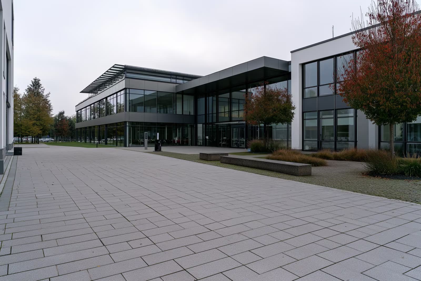 Un moderno edificio de una agencia de empleo alemana con un amplio patio pavimentado vacío bajo un cielo nublado.
