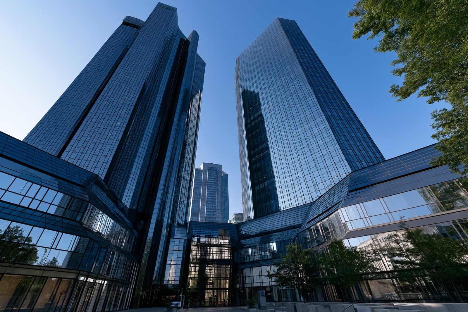 Dos torres bancarias gemelas de cristal en Frankfurt, que relucen contra un cielo azul brillante vistas desde abajo.